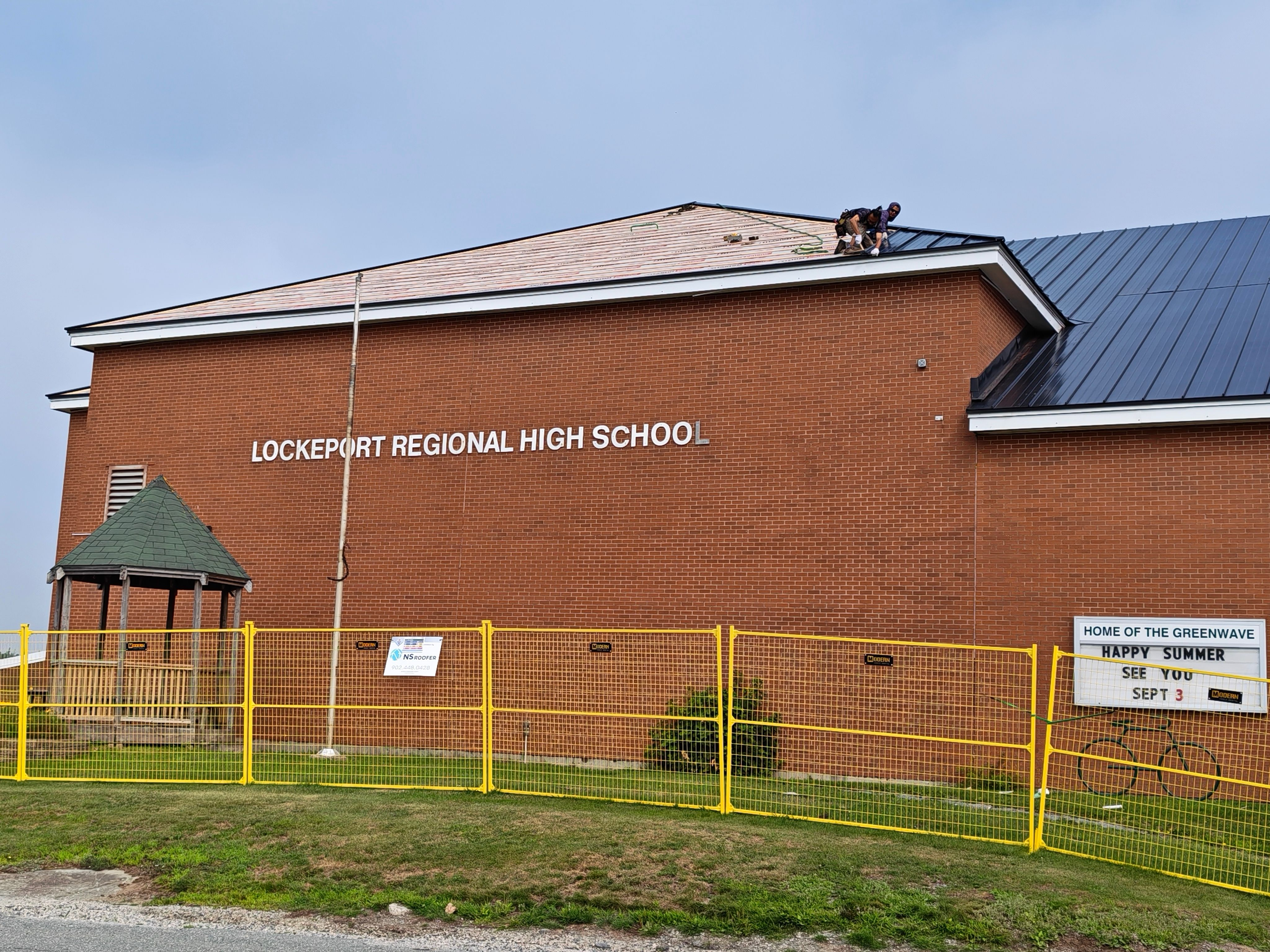 Metal roofing crew installing panels at Lockeport Regional High School